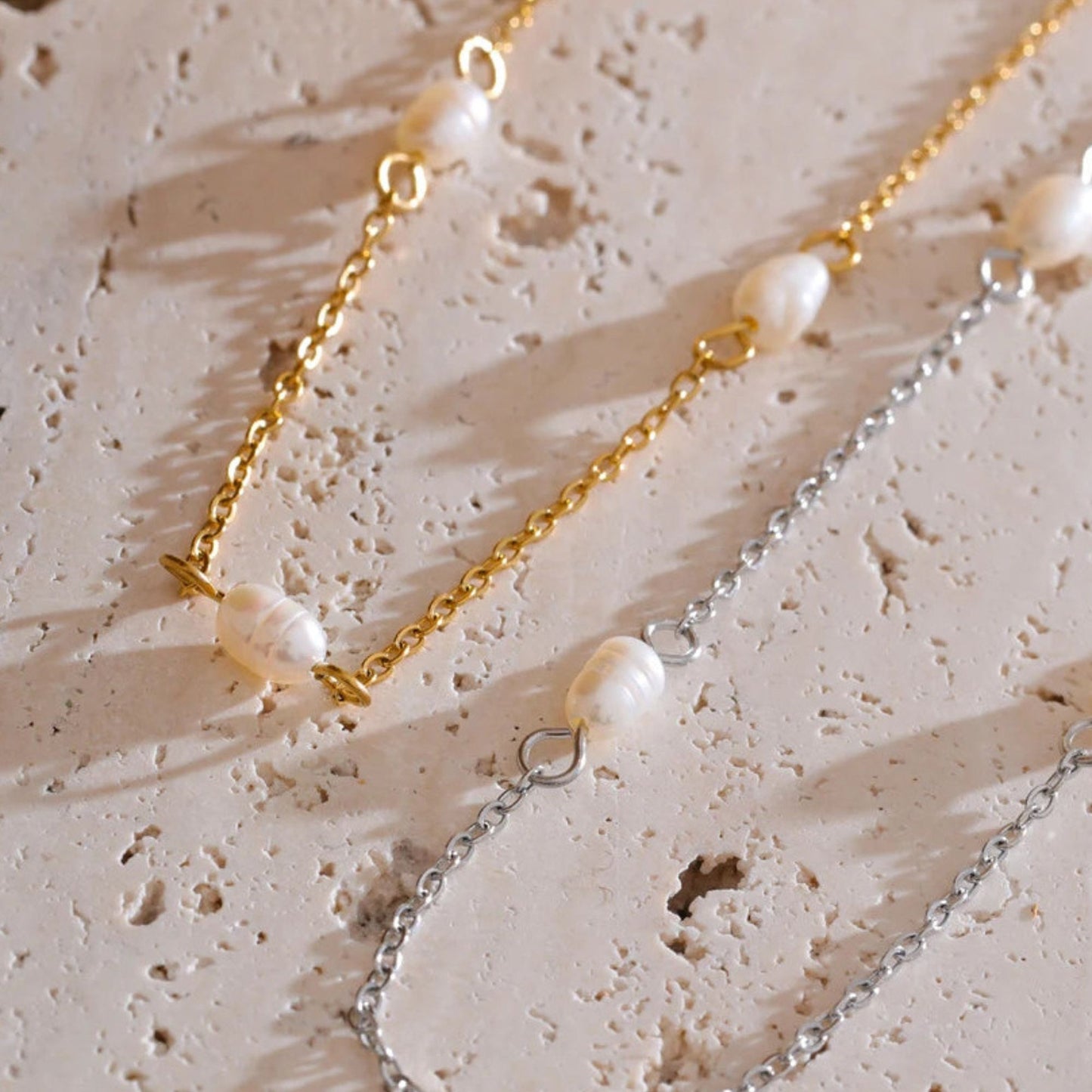 Two pearl necklaces, one stainless steel finish, the other one gold plated on a textured organic beige surface