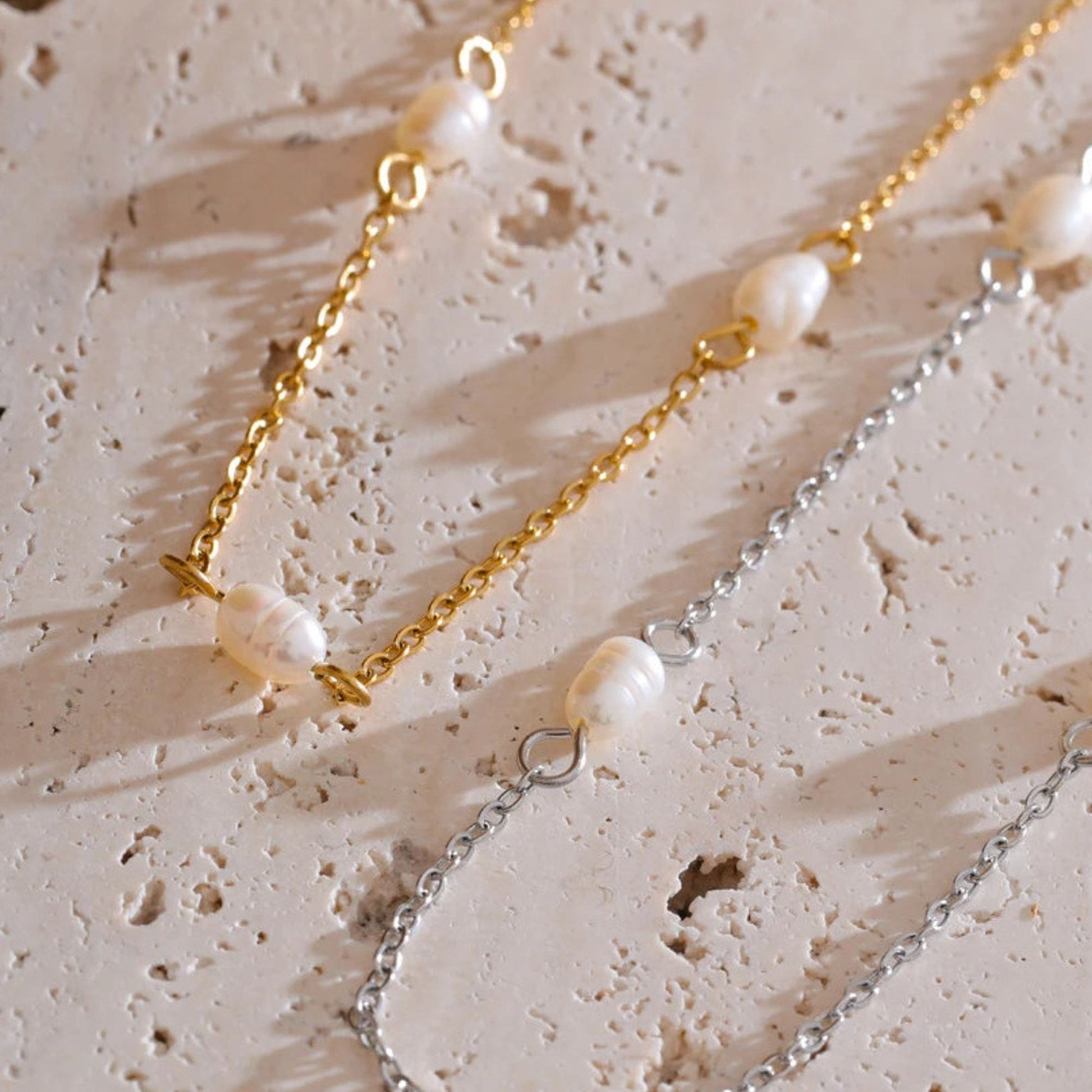 Two pearl necklaces, one stainless steel finish, the other one gold plated on a textured organic beige surface