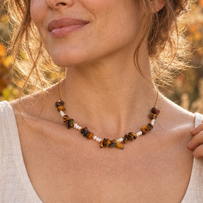 Woman in a linen top wearing a tiger stone and pearl chip necklace in an autumn garden