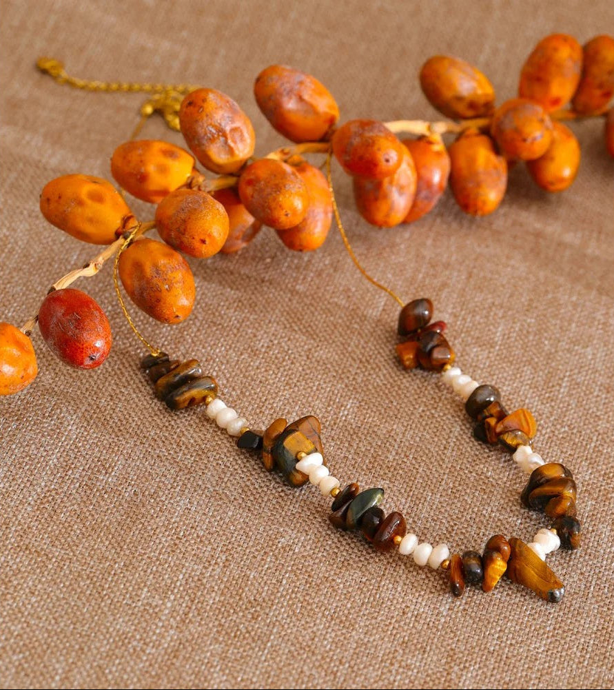 Tiger stone and pearl necklace on linen beside a branch of orange berries