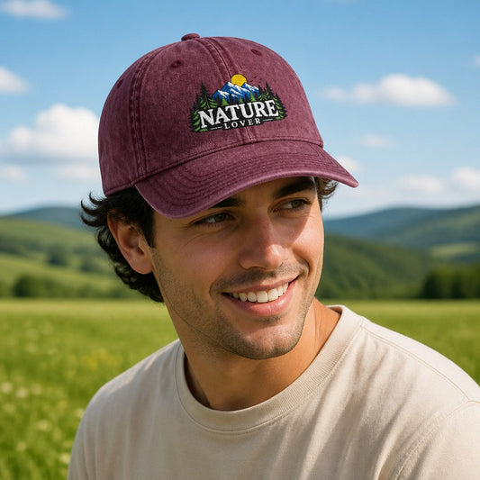 Man wearing a maroon retro-style Nature Lover baseball cap with embroidered mountain and sunrise design, standing in a scenic green field, outdoor enthusiasts, by Crossroads Dandelion