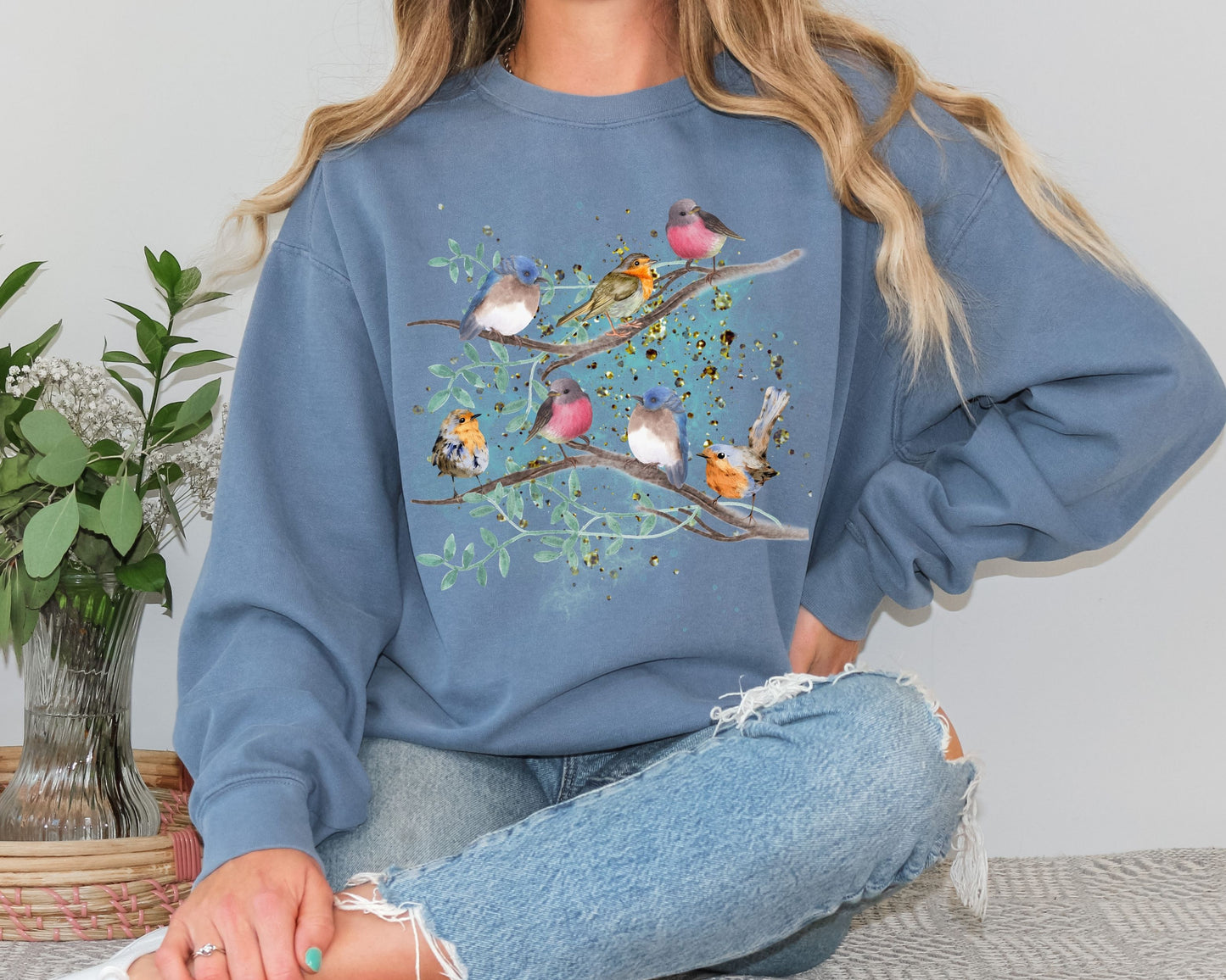 woman wearing a blue Jean color sweatshirt with a cute bird design sitting on a couch.