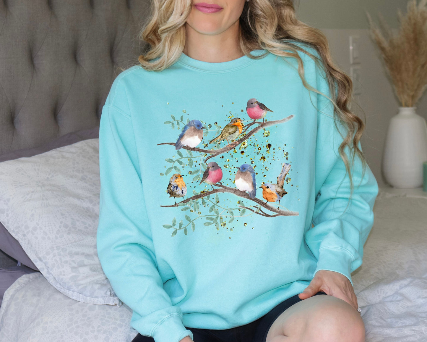 Woman wearing a chalky mint color sweatshirt with colorful birds and branches design