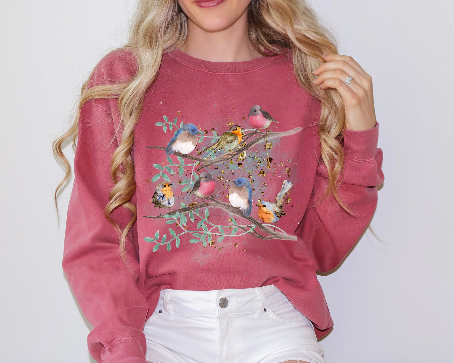 Blonde woman wearing a crimson color sweatshirt with a cute bird design on a plain background