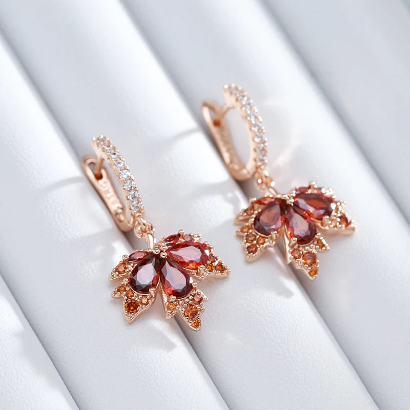 Close up of rose gold maple earrings with red gemstones on a white background