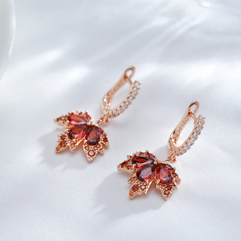 Close up of rose gold maple earrings with red gemstones on a white background