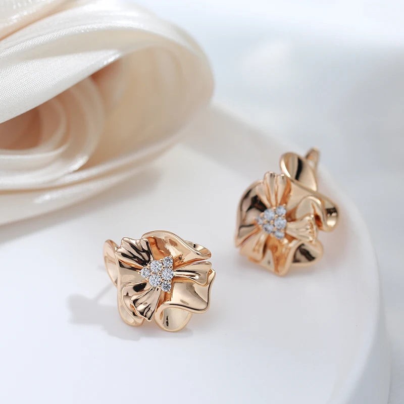 Pair of ruffled flower earrings on a white dish beside a cream satin rose