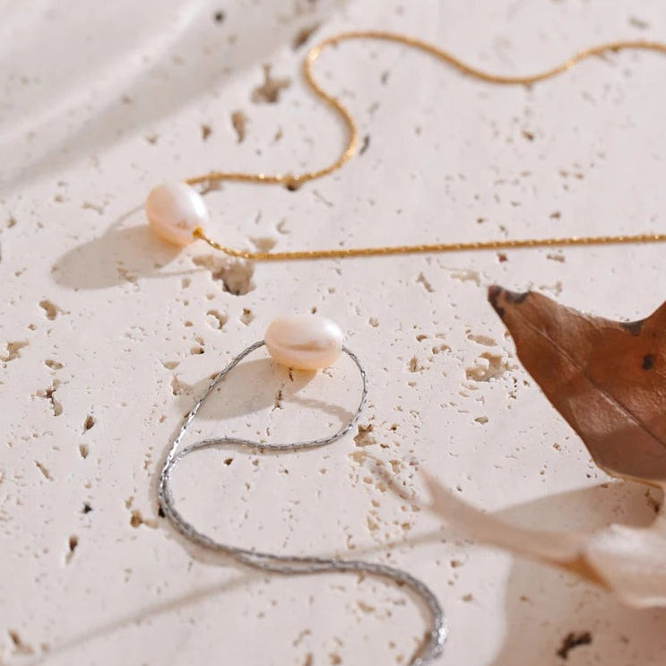 Gold and silver single pearl necklaces on travertine beside autumn leaves