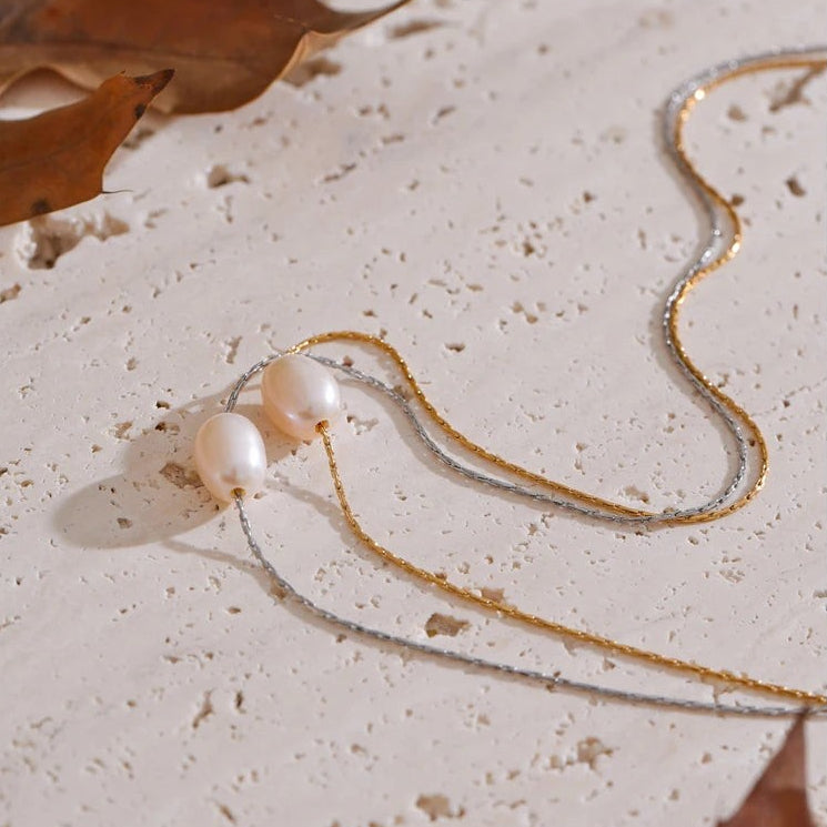 Gold and silver single pearl necklaces with their pearls side by side on stone