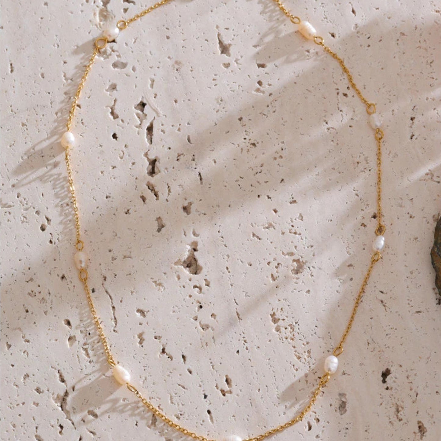 Gold station necklace with small pearls on a textured beige surface