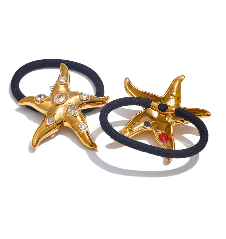 Two gold star-shaped hair ties with black elastic bands on a white background. One front view with white cubic zirconia, the other one back view with colorful cubic zirconia. 