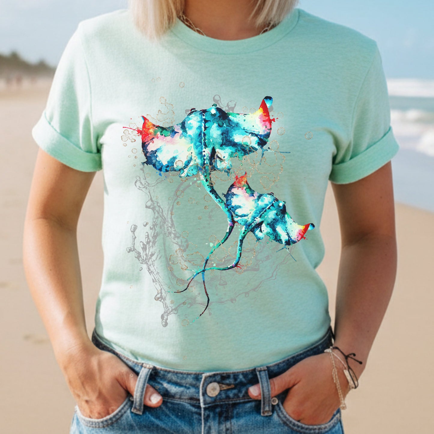 Woman wearing a heather mint t-shirt with a colorful stingray design on a beach.