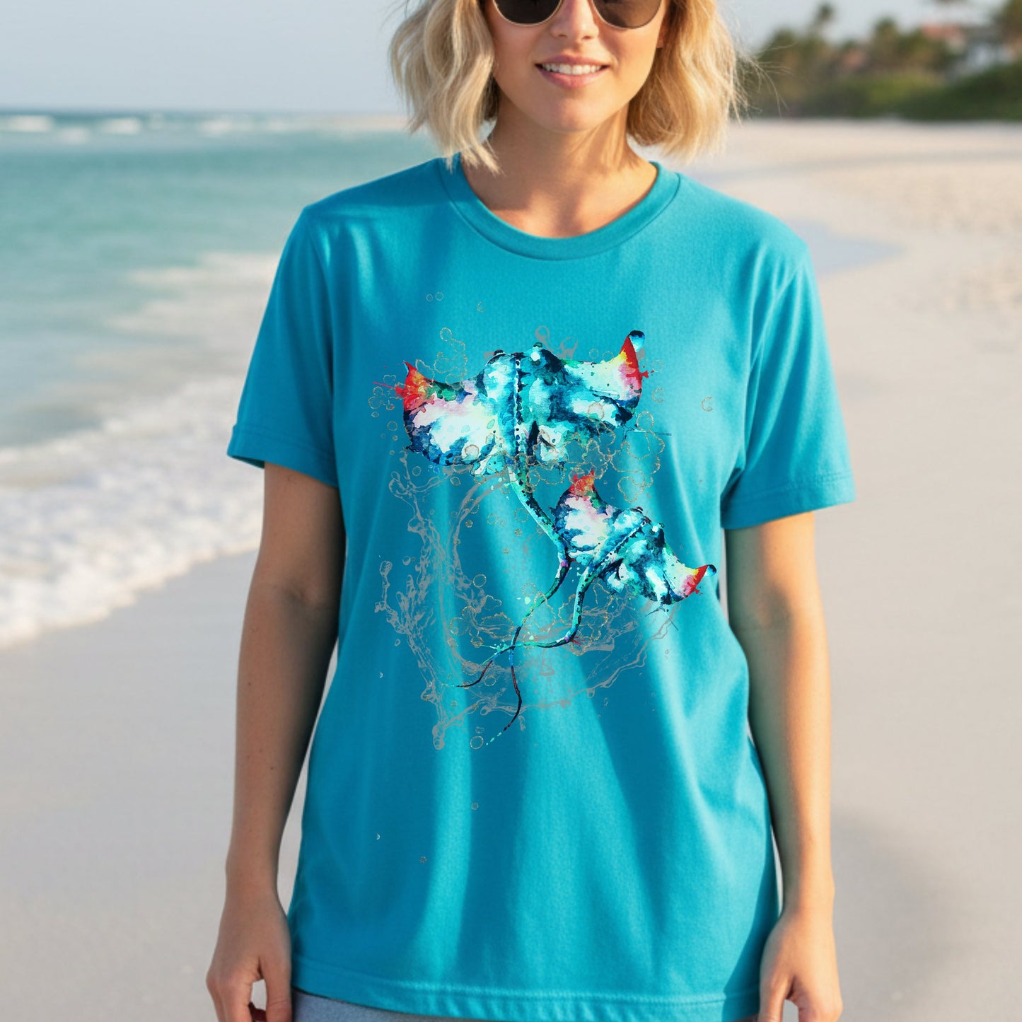 Woman wearing a turquoise t-shirt with a watercolor stingray design on a beach.