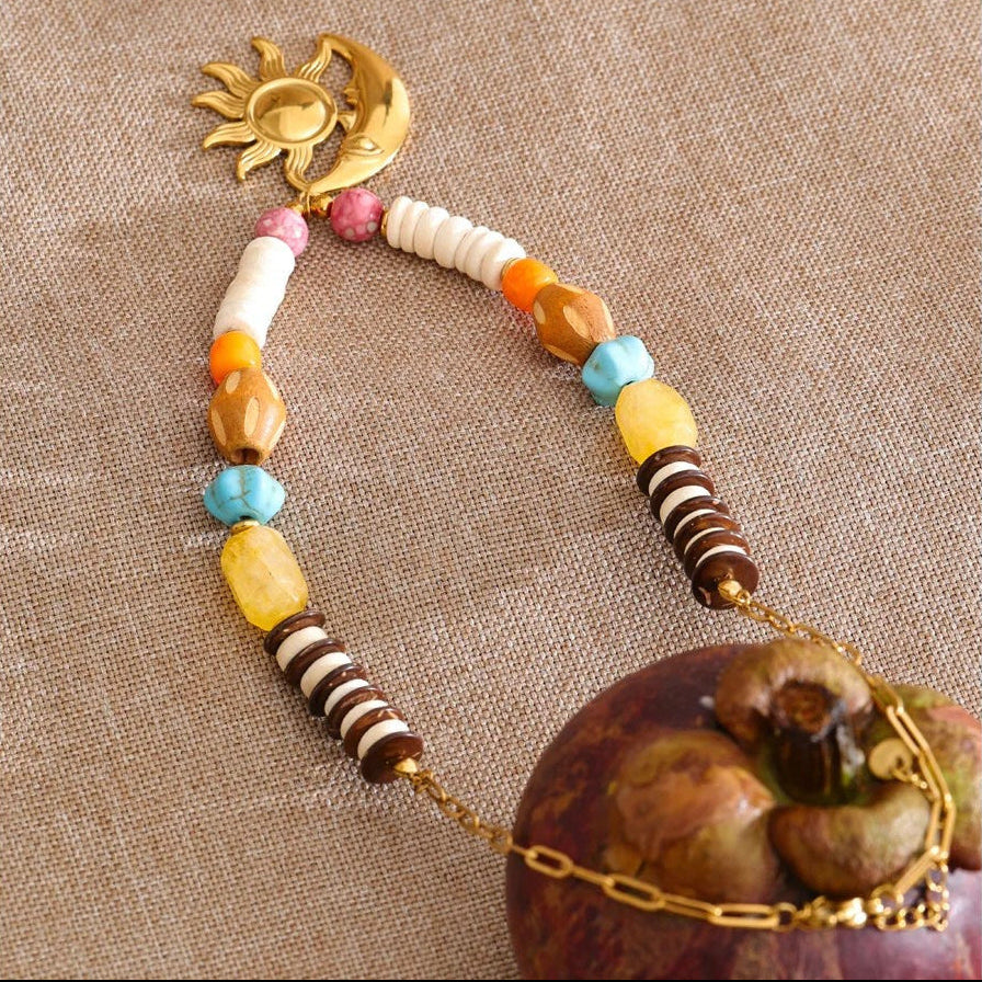 Colorful sun and moon beaded necklace on linen next to a piece of fruit