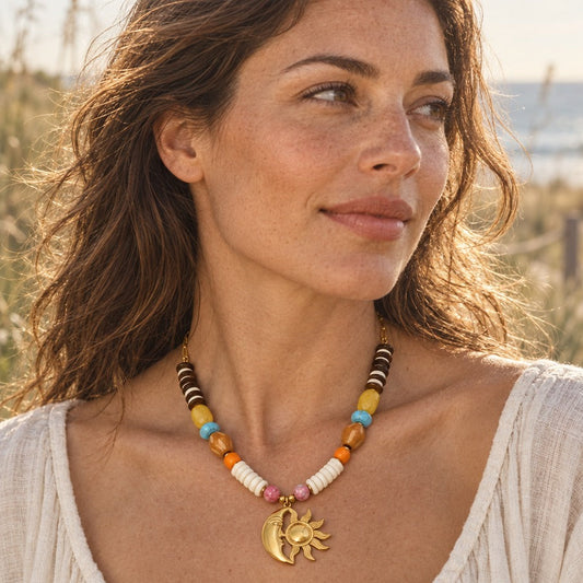 Woman in a cream linen top wearing a gold sun and moon beaded necklace on a sunlit beach path