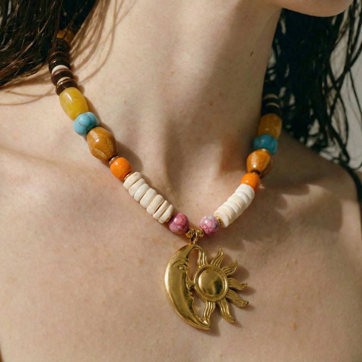 Close-up of a gold sun and moon pendant on a colorful beaded necklace worn at the collarbone