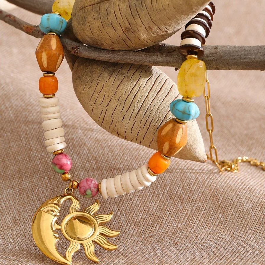 Sun and moon beaded necklace hanging from a branch against beige linen