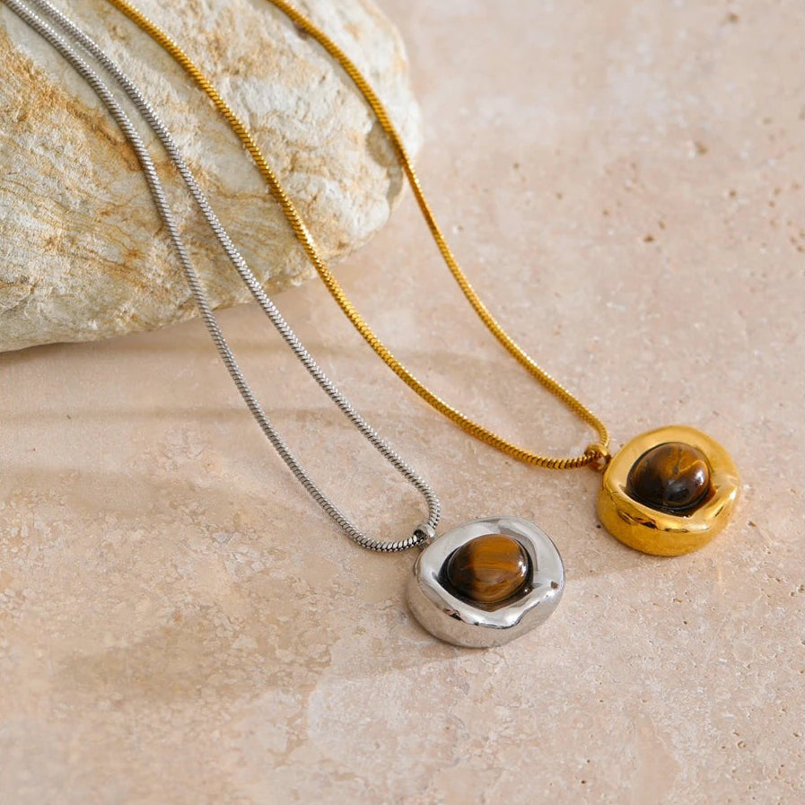 Gold and silver tiger eye pendant necklaces draped over a natural stone on travertine