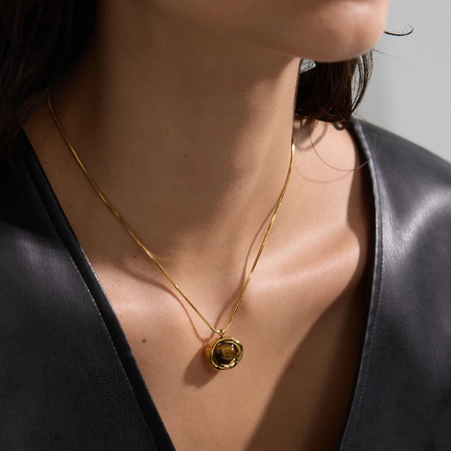 Woman in a dark leather top wearing a gold tiger eye pendant necklace