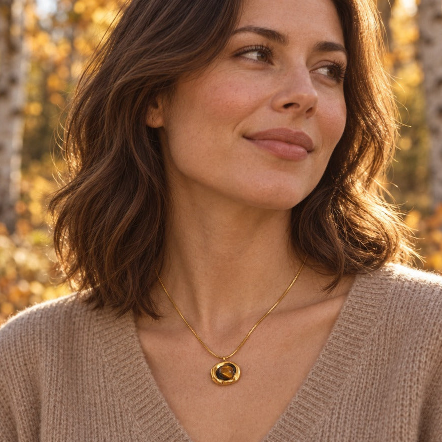 Woman in a camel knit wearing a gold tiger eye pendant necklace in an autumn birch woodland