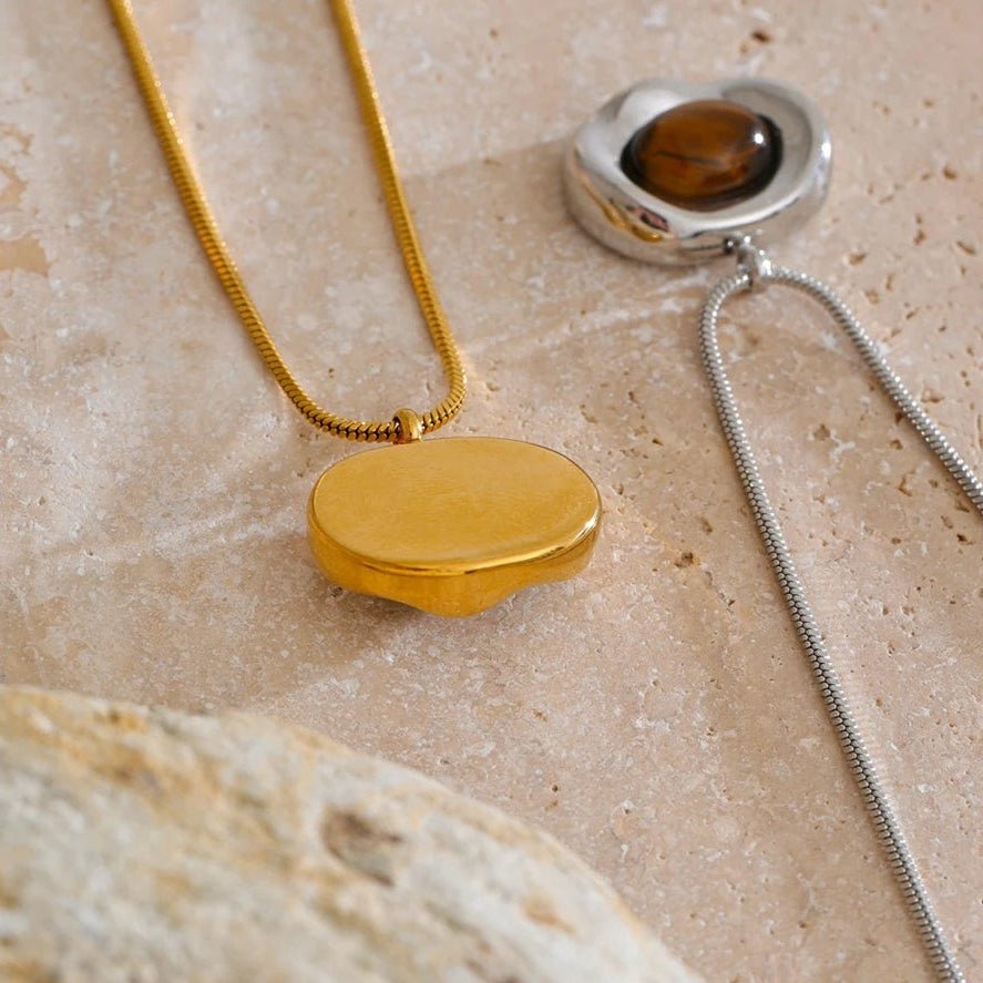 Polished gold back of the tiger eye pendant beside the silver version on travertine