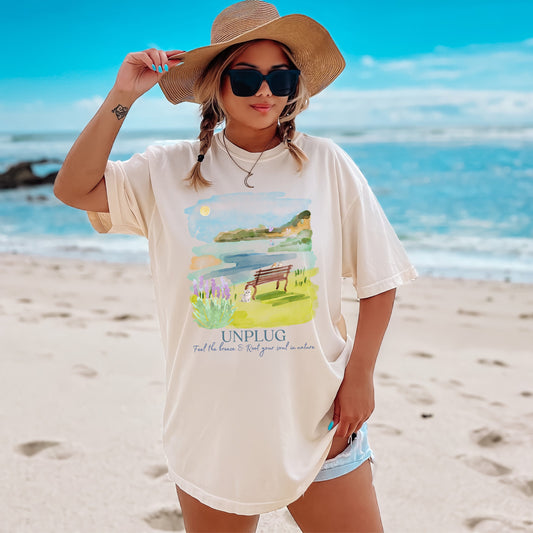 Woman on a beach wearing a t-shirt with a graphic design and text
Womens unplug nature shirt in Ivory – Comfort Colors watercolor lake scene tee by Crossroads Dandelion