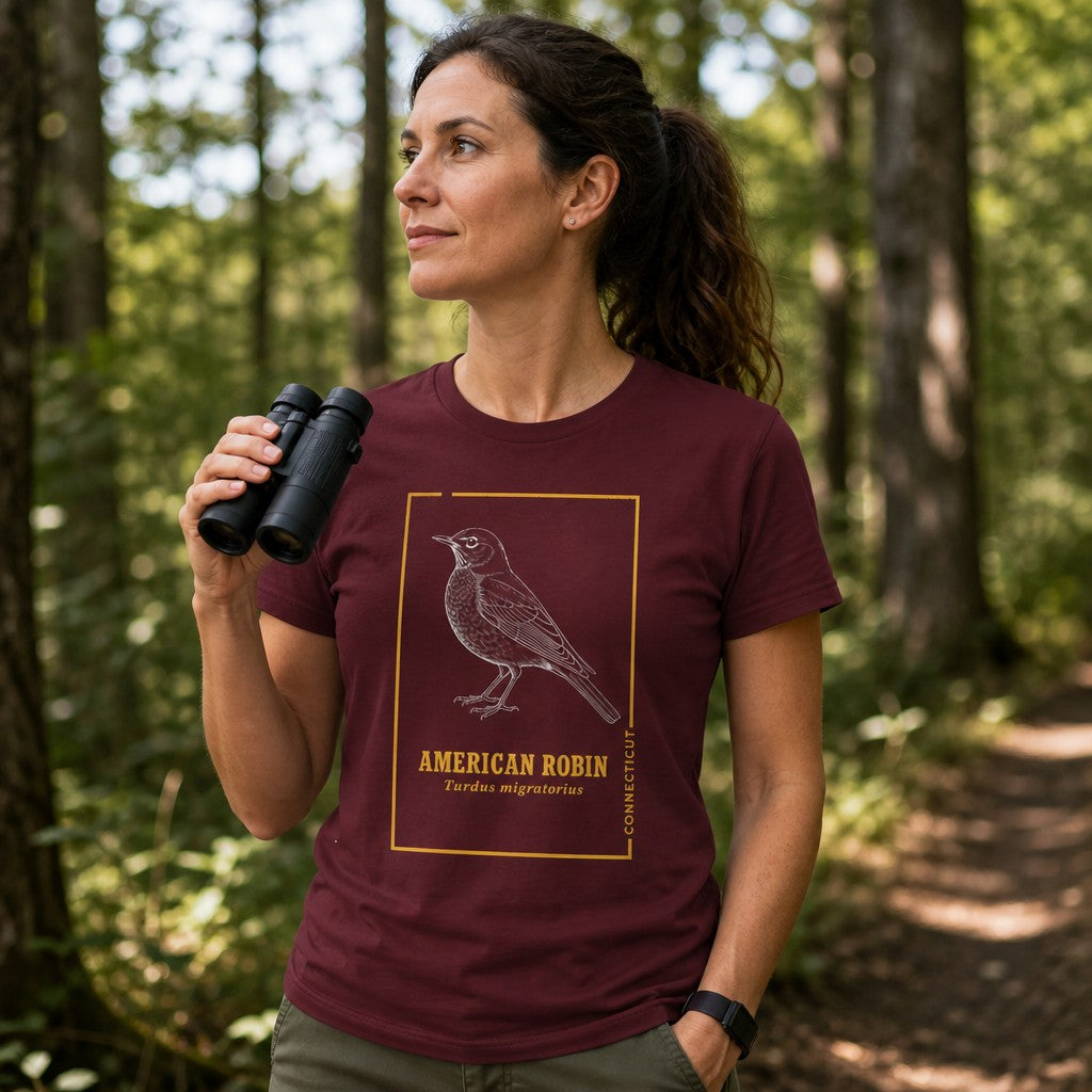 Woman in maroon Bella Canvas 3001 t-shirt featuring a vintage naturalist line art American Robin design with golden botanist trim, celebrating the Connecticut state bird, cottagecore style, birdwatching and nature lovers, hiking in woodland, by Crossroads Dandelion