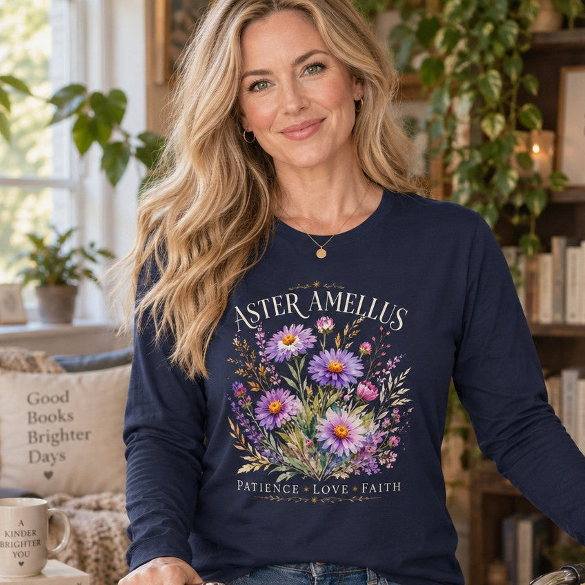Woman in a navy Bella Canvas® 3501 long sleeve shirt featuring a vintage botanical bouquet of aster and amellus flowers in soft lavender, pink, and violet hues with gold wheat accents, cream serif text and inspirational words, romantic cottagecore style, cozy reading nook scene, floral nature enthusiasts, by Crossroads Dandelion