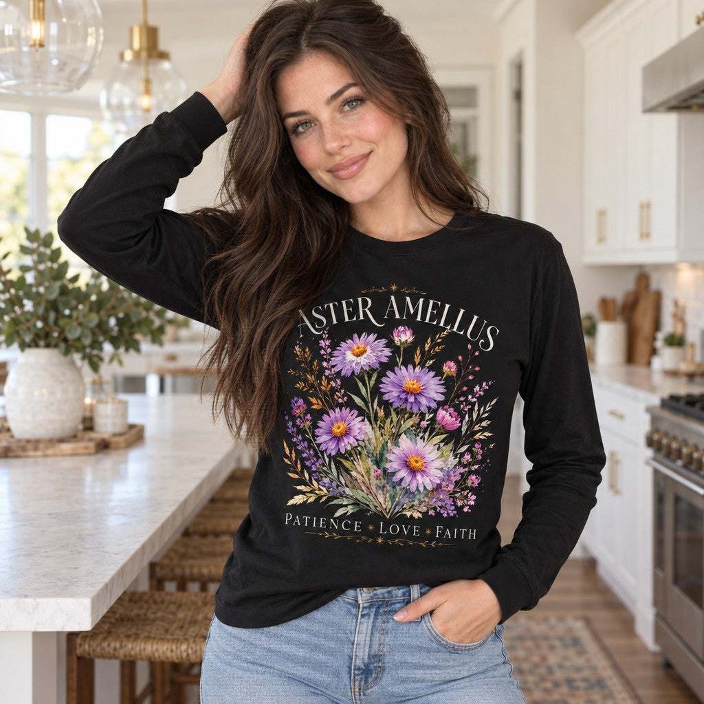 Woman in black Bella Canvas® 3501 long sleeve featuring a vintage romantic botanical design with hand-painted aster and amellus flowers, soft lavender, pink and violet hues, golden wheat, cream serif text 'ASTER AMELLUS', and words 'PATIENCE LOVE FAITH', photographed in a bright kitchen, floral nature lovers, by Crossroads Dandelion
