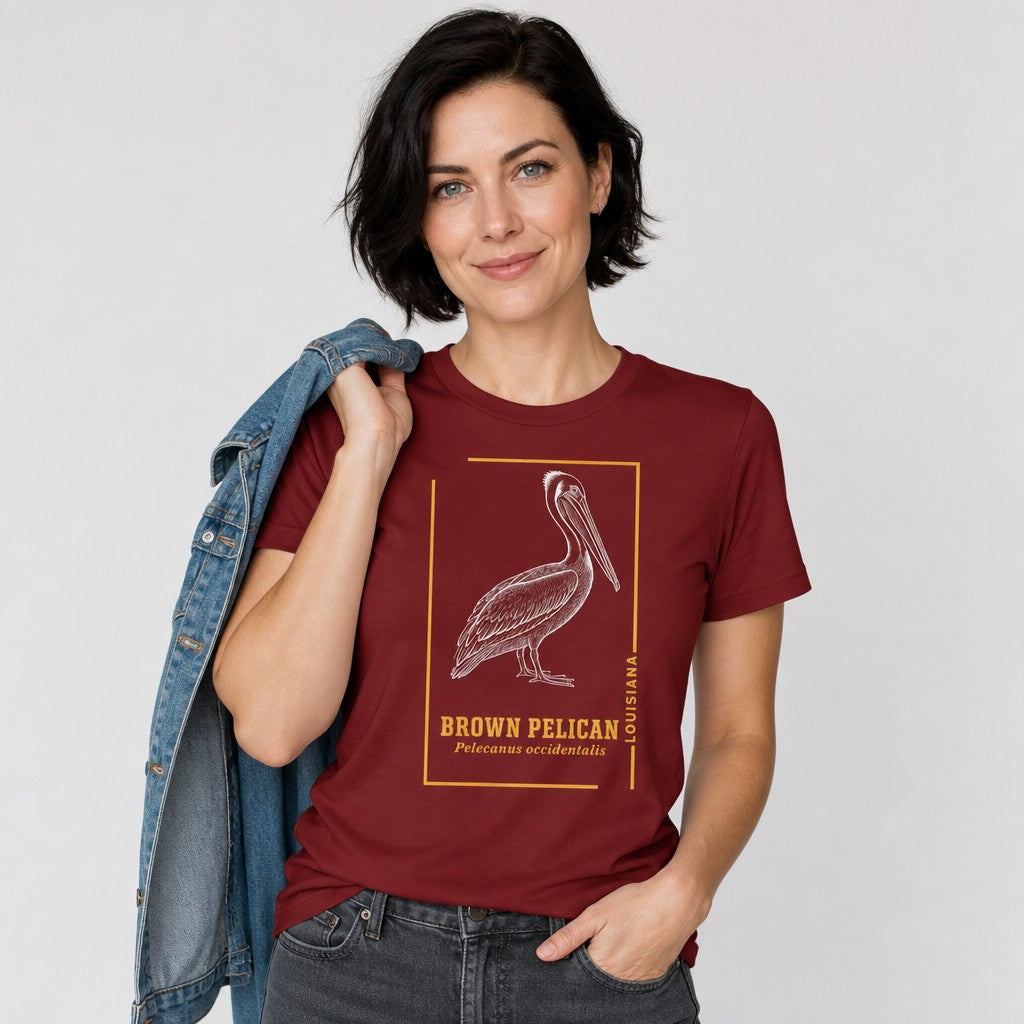 Woman wearing cardinal red Bella Canvas 3001 t-shirt featuring vintage engraving style brown pelican illustration framed in golden ochre linework, ideal for birdwatchers and nature lovers, classic heritage design, by Crossroads Dandelion