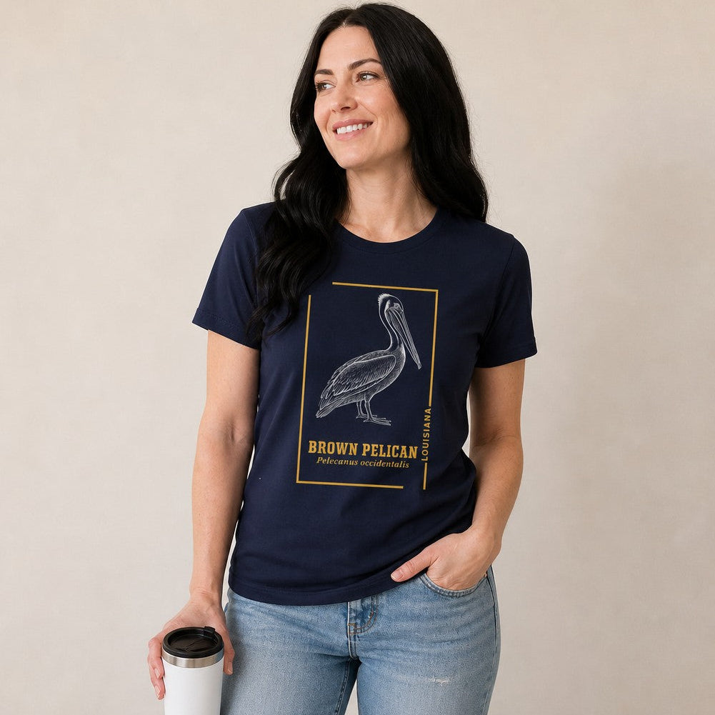 Woman wearing a navy Bella Canvas 3001 t-shirt featuring a vintage engraving of a brown pelican framed in golden ochre linework, ideal for birdwatchers and naturalists, classic coastal style, by Crossroads Dandelion