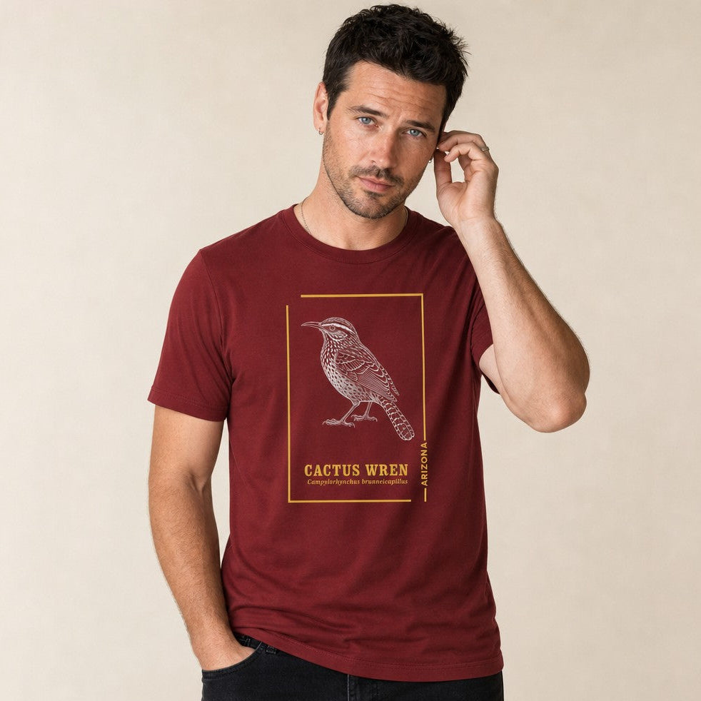 Man wearing cardinal red Bella Canvas 3001 t-shirt featuring a vintage hand-drawn line art of the Cactus Wren, Arizona state bird, accented with golden botanical frames, ideal for bird and desert nature lovers, vintage style, by Crossroads Dandelion