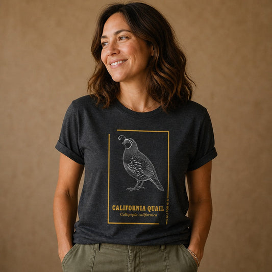 Woman wearing a dark grey heather Bella Canvas 3001 t-shirt with a vintage hand-drawn California quail illustration bordered with golden botanical accents, ideal for birdwatchers and California wildlife lovers, indoor setting, by Crossroads Dandelion