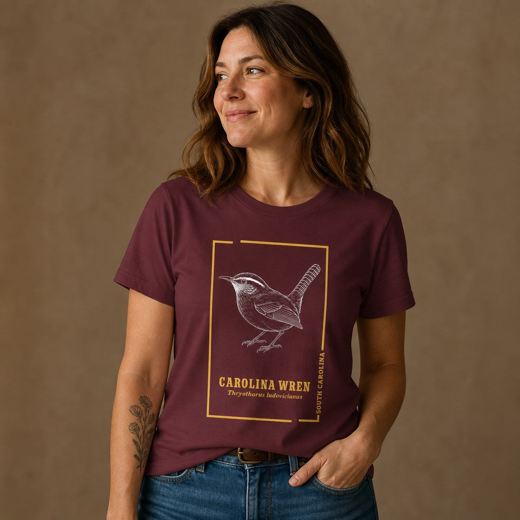 Woman wearing a maroon Bella Canvas 3001 t-shirt with a vintage hand-drawn Carolina Wren and golden frame design, cottagecore style naturalist field sketch for bird lovers and wildlife artists, by Crossroads Dandelion