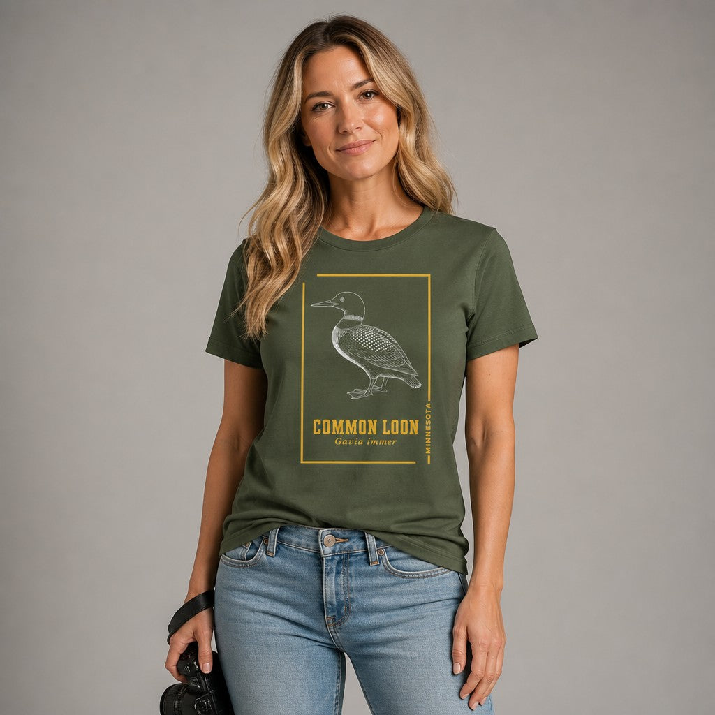 Woman in military green Bella Canvas 3001 t-shirt featuring a vintage-inspired black and white etching of a common loon with gold accent borders, ideal for birdwatchers, wildlife fans, and cottagecore enthusiasts, by Crossroads Dandelion