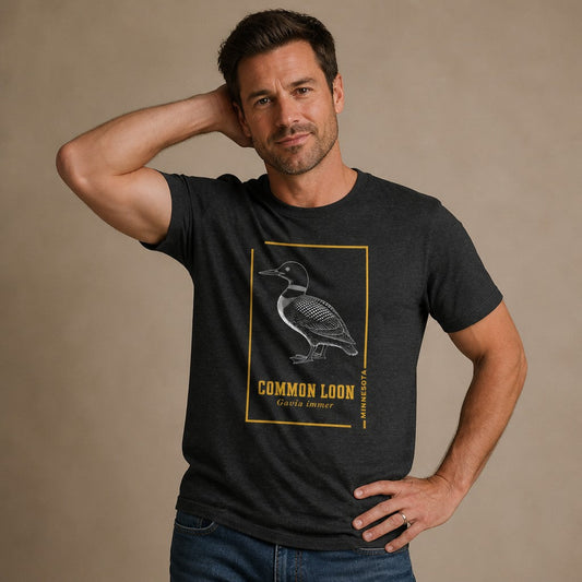 Man wearing a dark grey heather Bella Canvas 3001 t-shirt with a vintage etching of a common loon, Minnesota state bird, accented by gold borders and classic type, perfect for birdwatchers and fans of cottagecore naturalist design, by Crossroads Dandelion