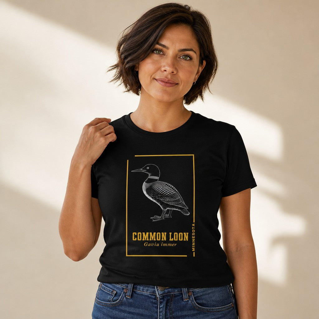 Woman wearing a black Bella Canvas 3001 t-shirt with a vintage-inspired etching of a common loon, Minnesota state bird, in black and white with gold accent borders, evoking classic naturalist journals, cottagecore birdwatcher style, for wildlife lovers, by Crossroads Dandelion
