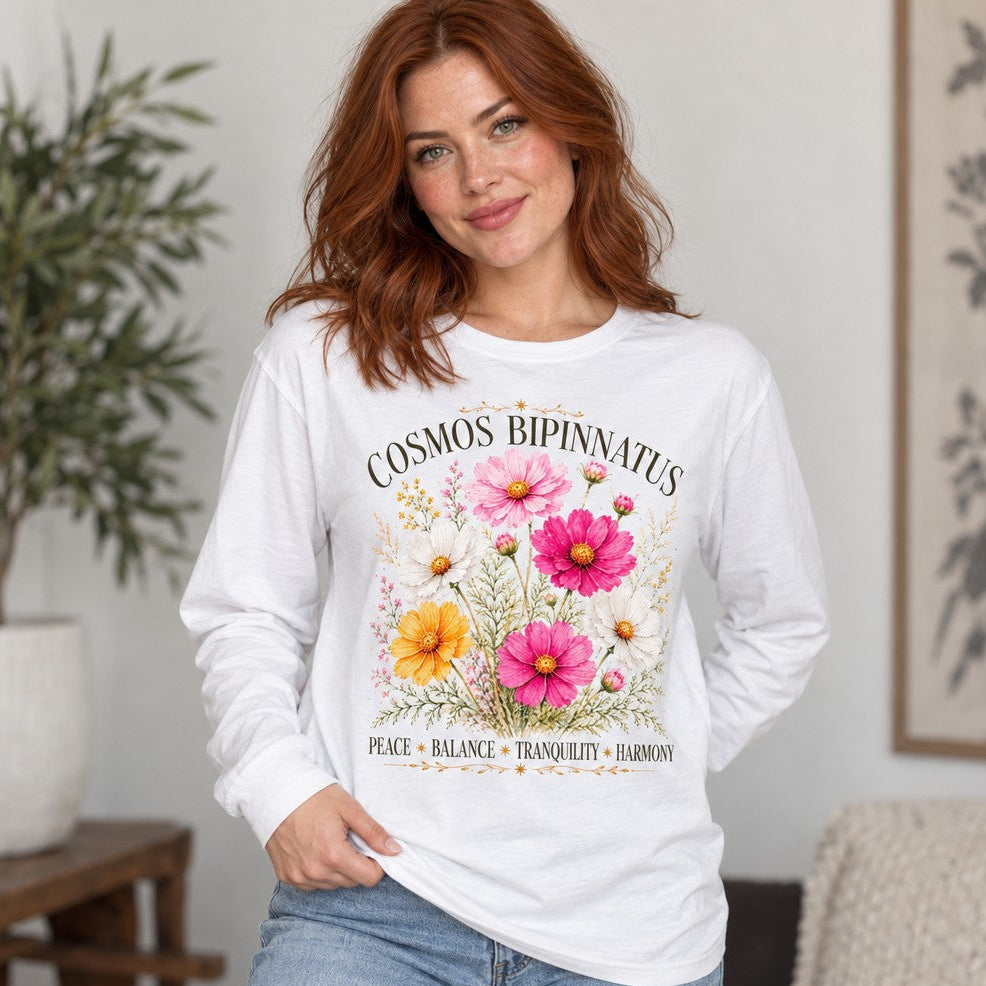 Woman in white Bella Canvas 3501 long sleeve shirt featuring a vintage-style hand-drawn Cosmos bipinnatus floral design in pink, yellow, magenta and white, framed with golden botanical flourishes and calm affirmations, perfect for boho-chic and nature lovers, by Crossroads Dandelion