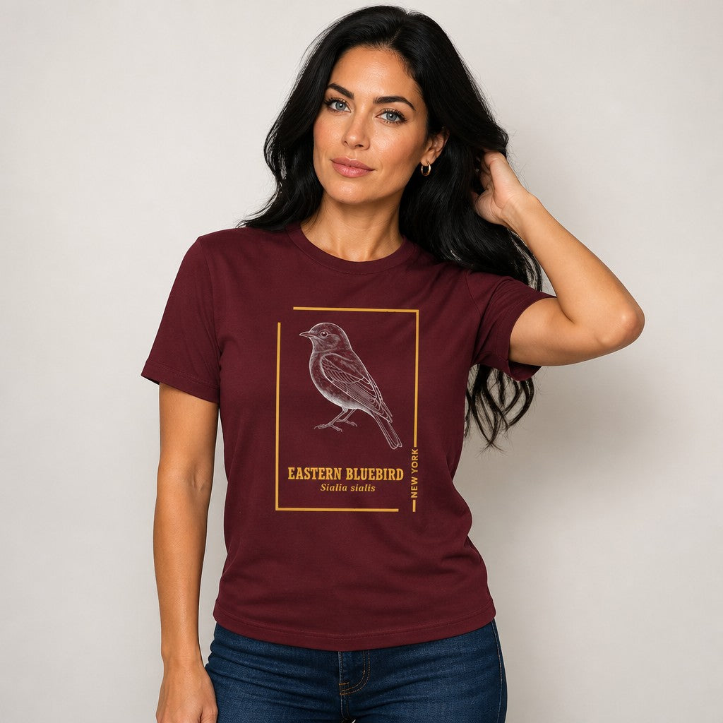 Woman wearing a maroon Bella Canvas 3001 t-shirt featuring a hand-drawn vintage Eastern Bluebird in gold-framed line art with classic typography, minimalist cottagecore wildlife design, perfect for women who love retro and nature-inspired apparel, by Crossroads Dandelion