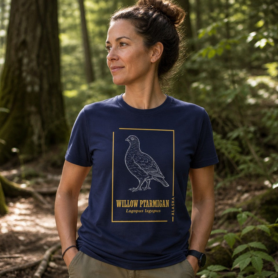 Woman wearing a navy Bella Canvas 3001 t-shirt featuring a hand-drawn, vintage-style willow ptarmigan illustration with golden botanical accents, inspired by naturalist field journals, perfect for birdwatchers and cottagecore enthusiasts, forest hike scene, by Crossroads Dandelion