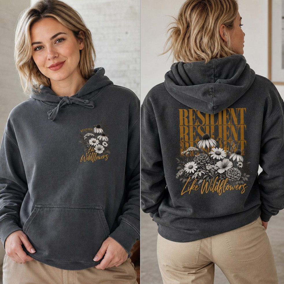 Woman wearing a pepper-colored vintage-style hoodie featuring a hand-drawn resilient wildflowers design with bold typography, photographed in a relaxed indoor setting, casual women's fashion, by Crossroads Dandelion