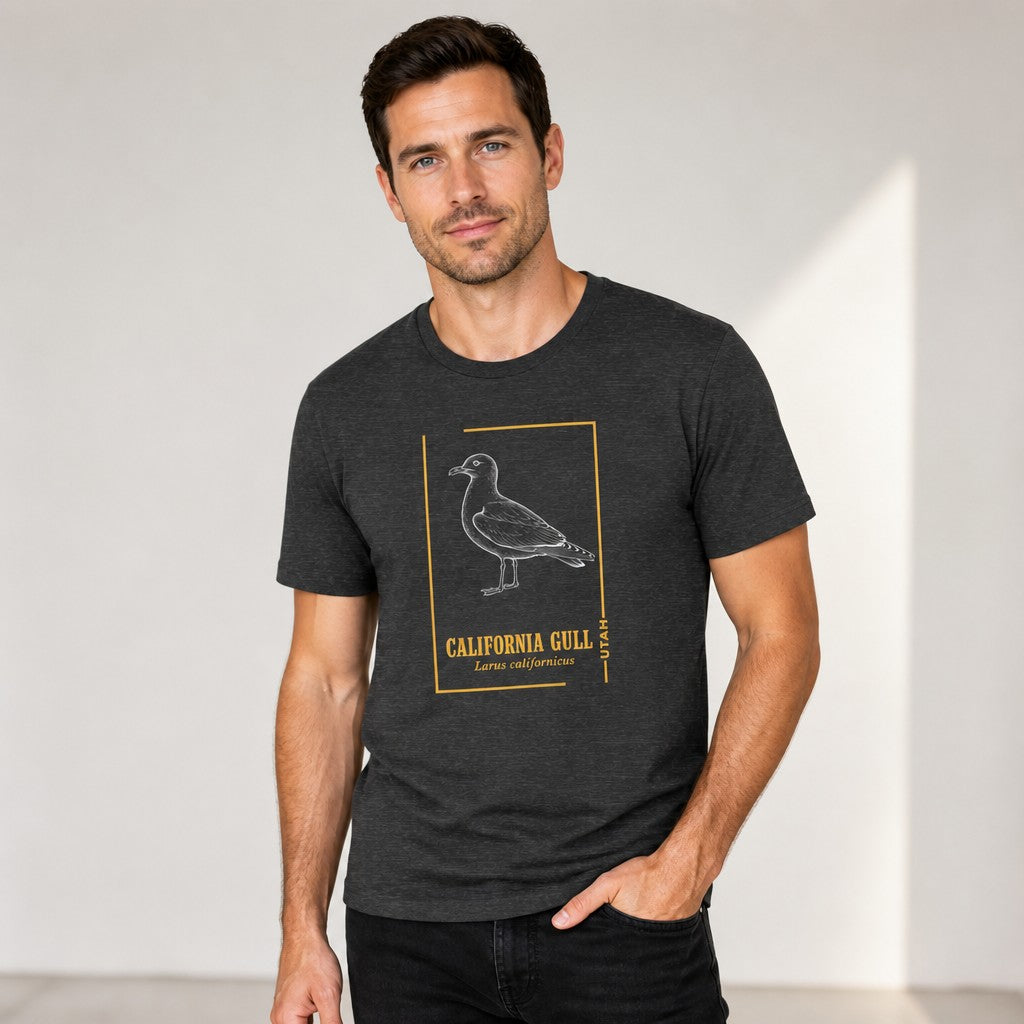 Man wearing a dark grey heather Bella Canvas 3001 t-shirt featuring a vintage line art illustration of the California Gull with golden botanical accents, ideal for birdwatchers and wildlife art lovers, studio setting, by Crossroads Dandelion
