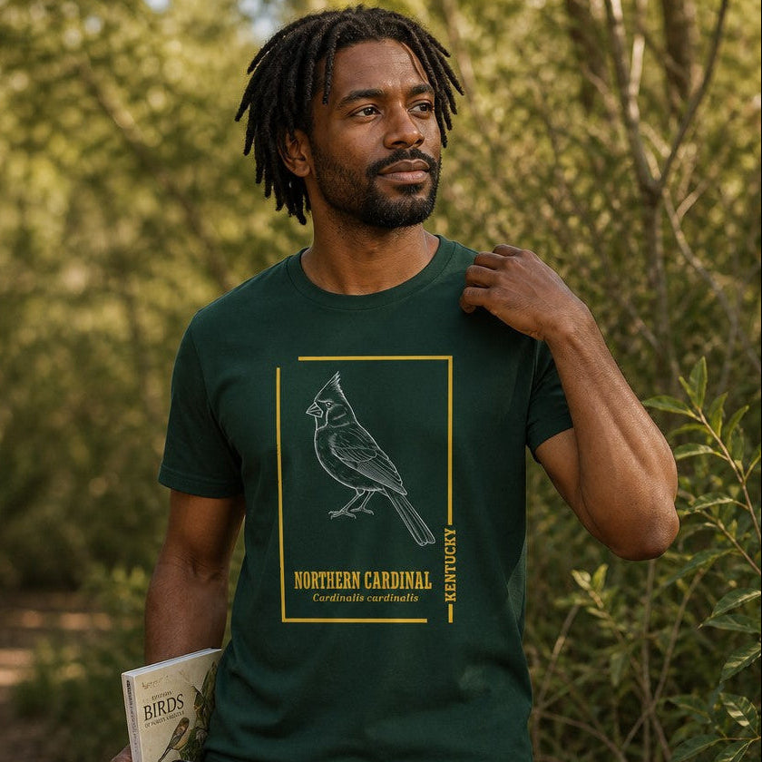 Man in forest green Bella Canvas 3001 t-shirt featuring a vintage hand-drawn white line Northern Cardinal illustration with gold border and botanical typography, ideal for birdwatchers and nature lovers, hiking in the woods, by Crossroads Dandelion