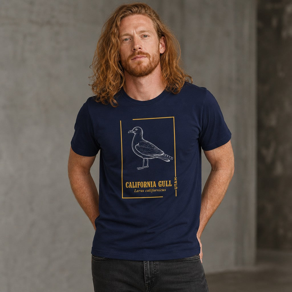 Man wearing navy Bella Canvas 3001 t-shirt with vintage-style line art of a California Gull in chalk-white, gold botanical accents, classic nature print aesthetic for birdwatchers and naturalists, indoors, by Crossroads Dandelion