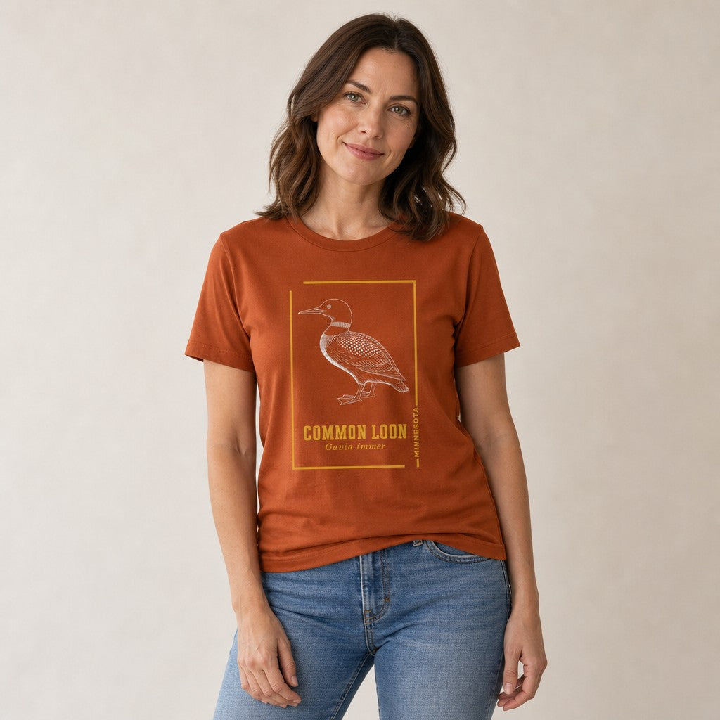 Woman in autumn orange Bella Canvas 3001 t-shirt featuring a vintage line art etching of a common loon, Minnesota state bird, with gold accent borders and classic typography, perfect for birdwatchers, wildlife lovers, and cottagecore fans, by Crossroads Dandelion