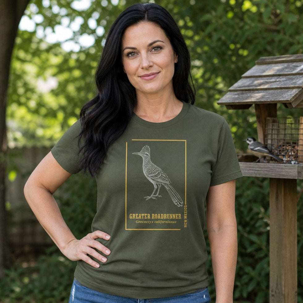Woman in military green Bella Canvas 3001 t-shirt featuring a vintage-inspired white line art illustration of a Greater Roadrunner with golden botanical accents, standing outdoors by a bird feeder, perfect for birdwatchers, nature lovers, cottagecore and wildlife print fans, by Crossroads Dandelion