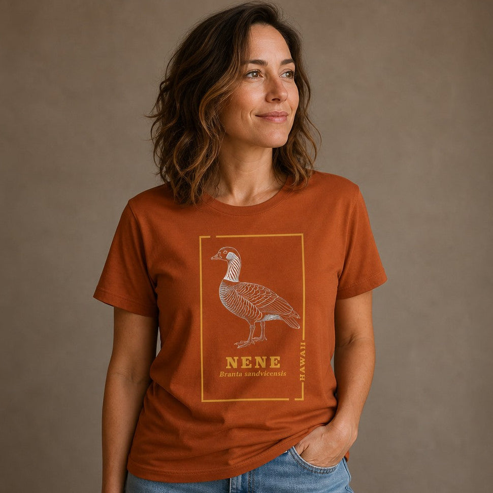 Woman wearing an autumn Bella Canvas 3001 t-shirt with a vintage line art illustration of a nene goose, framed by golden botanical borders, celebrating Hawaii's state bird, perfect for birdwatchers and nature lovers, by Crossroads Dandelion