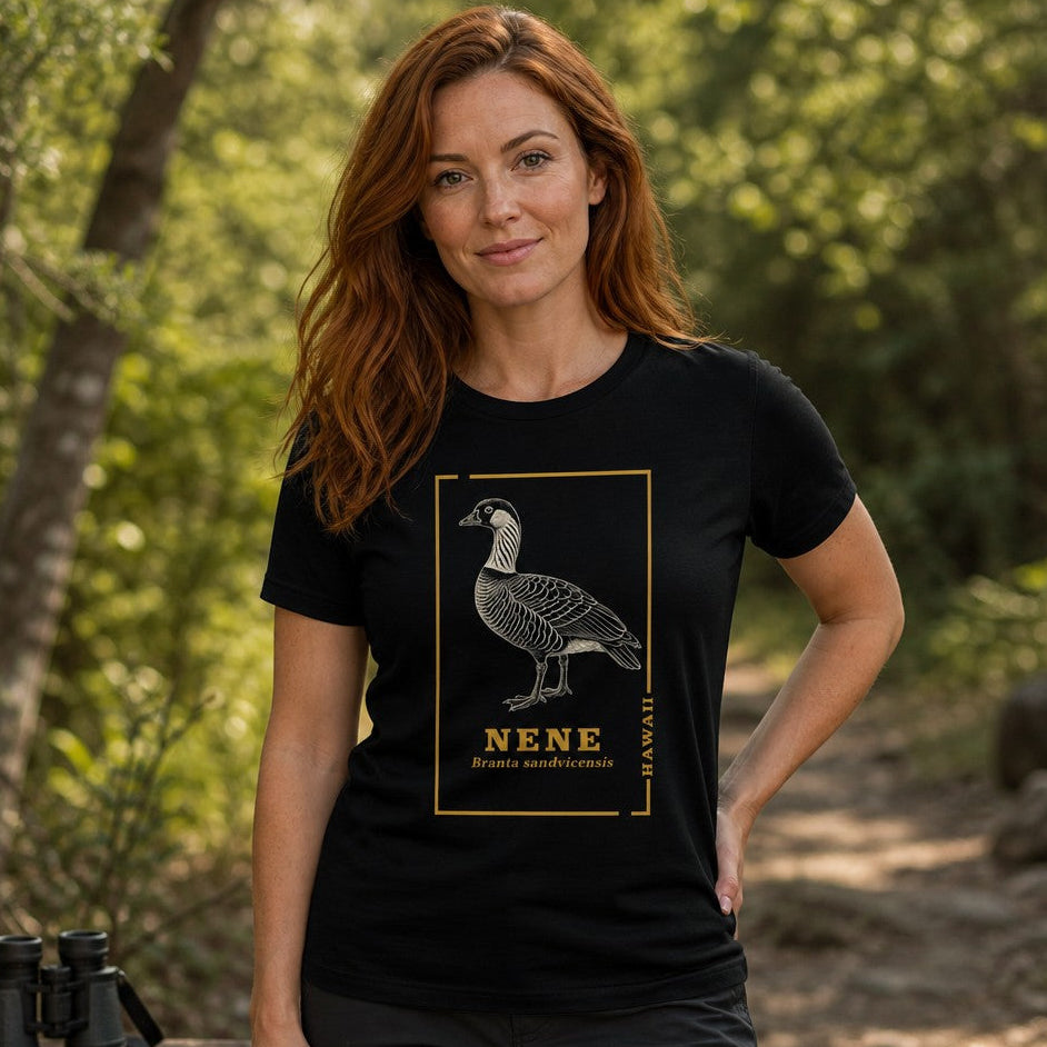 Woman wearing a black Bella Canvas 3001 t-shirt featuring a vintage line art illustration of the Hawaiian nene goose with golden botanical borders, naturalist hand-drawn style, on a forest trail, perfect for birdwatchers and nature lovers, by Crossroads Dandelion