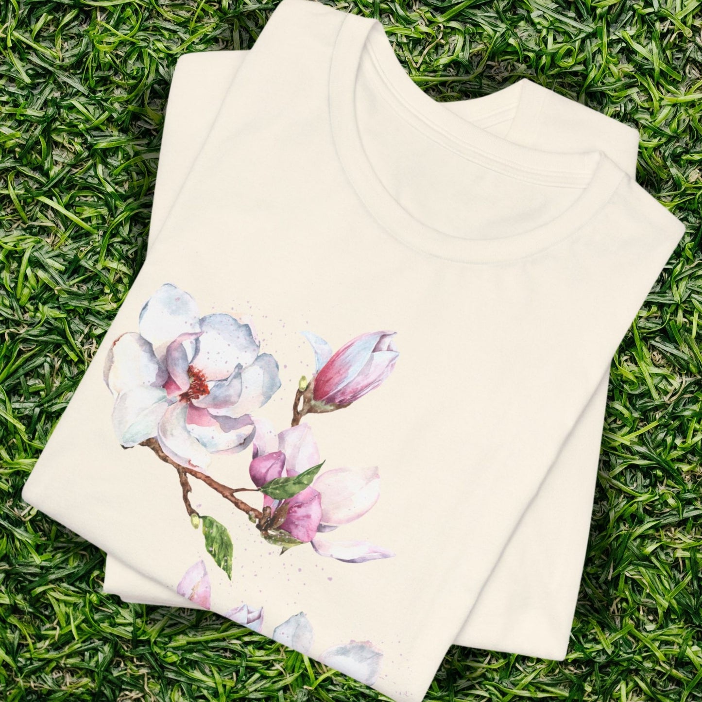 Folded natural color t-shirt with watercolor magnolia blossom and botanical floral design by Crossroads Dandelion

