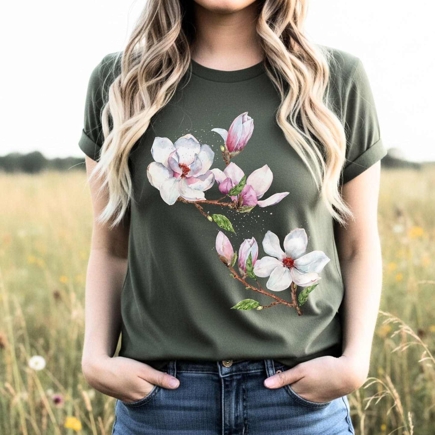 Woman wearing a military green vintage magnolia tee with watercolor floral design in a meadow by Crossroads Dandelion

